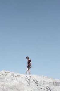 Low angle view of woman on rock against clear blue sky