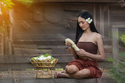 Young woman in traditional clothing holding flowers while sitting outdoors