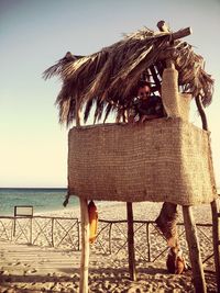 Portrait of man sitting in hut at beach against clear sky