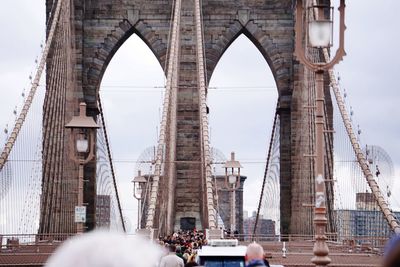 People on brooklyn bridge against cloudy sky