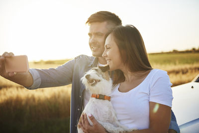 Young couple kissing dog against sky