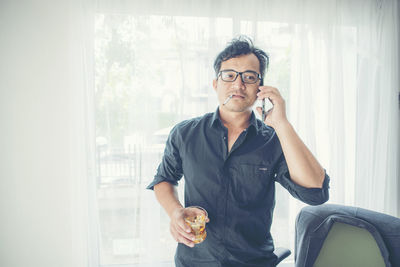 Young man using phone while standing by window at home