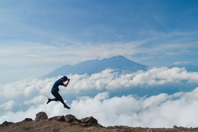 Side view of hiker jumping on mountain peak against sky