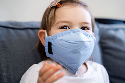 Portrait of baby girl wearing mask sitting on sofa at home