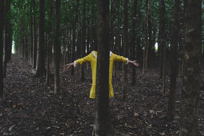 Man standing by tree trunk in forest