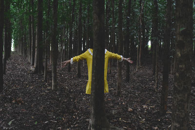 Woman standing by tree trunk in forest