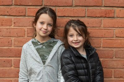 Portrait of smiling siblings standing against brick wall