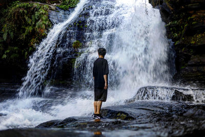 Rear view of man standing against waterfall