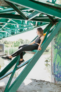 Full length of young woman sitting on railway bridge