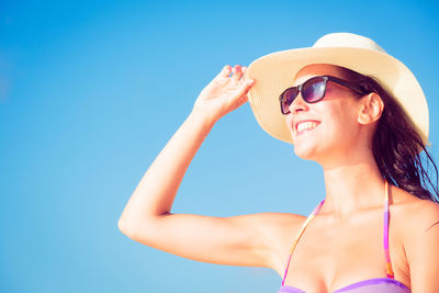 Close-up of young woman wearing sunglasses against clear blue sky