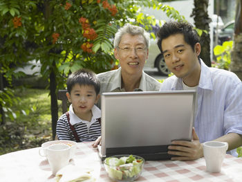 Portrait of smiling family using laptop at back yard