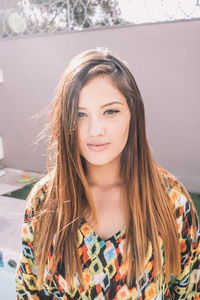 Portrait of woman with long brown hair against wall