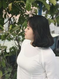 Side view of young woman standing against plants