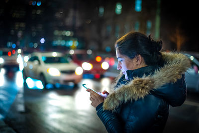 Woman holding mobile phone on street in city during winter