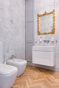 Toilet with gold large mirror, concrete walls and wooden parquet on the floor