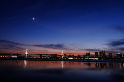 Illuminated city by river against sky at night