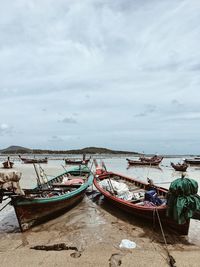 Fishing boats moored on sea shore against sky