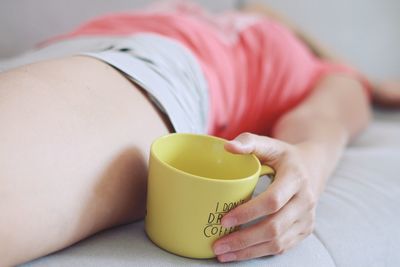Close-up of woman holding cup on bed at home