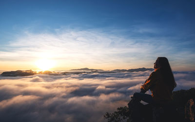 A female traveler sitting on the mountain peak, watching sunrise and sea of fog