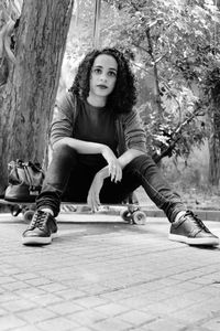 Portrait of young woman sitting on tree trunk in park