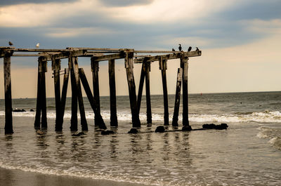 Abandoned wooden pier at beach against sky