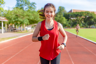 Portrait of smiling young woman running on track
