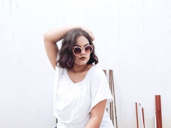 Woman wearing sunglasses posing against white wall