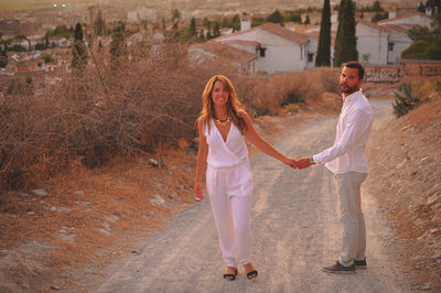 Full length of young couple on dirt road in city at sunset