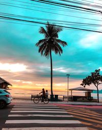 People riding bicycle on road against sky during sunset