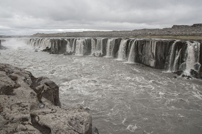 Scenic view of waterfall by sea against sky