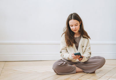 Young woman using phone while sitting on wooden floor