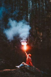Woman holding distress flare while sitting in forest