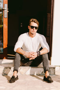 Full length of young man wearing sunglasses sitting outdoors