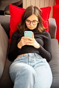 Young woman using mobile phone while sitting on sofa