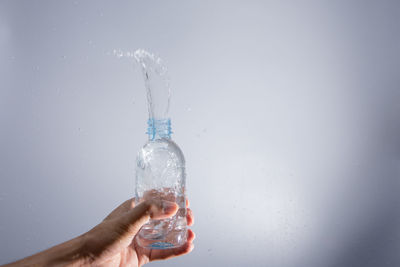 Cropped hand splashing water from bottle against gray background