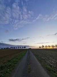 Empty road amidst field against sky