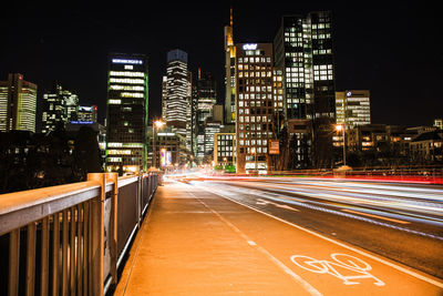 Light trails on city street by illuminated buildings at night