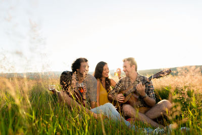 Friends sitting on grassy land against sky
