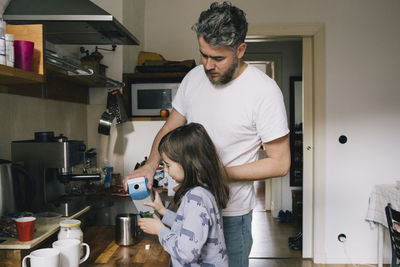 Father and daughter pouring milk in container at kitchen counter