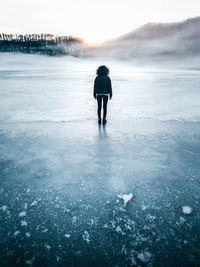 Full length rear view of woman standing on frozen lake