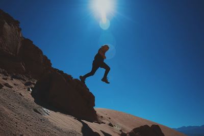 Low angle view of man jumping over desert on sunny day