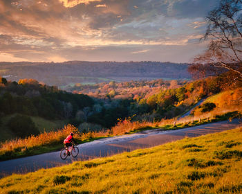 Man riding bicycle on mountain against sky during sunset