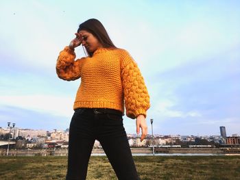 Smiling young woman in sweater against sky
