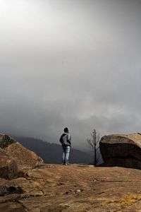 Rear view of man standing on rock against sky