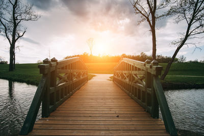 Wooden bridge over lake against sky during sunset