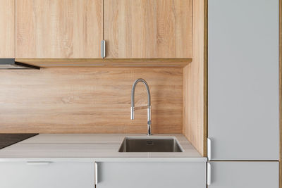 Metal sink and faucet at contemporary minimal kitchen. wooden furniture at  refurbished apartment