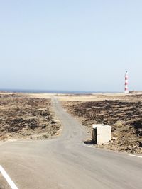 Lighthouse on road by sea against clear sky