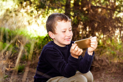 Smiling boy holding mobile phone while sitting outdoors