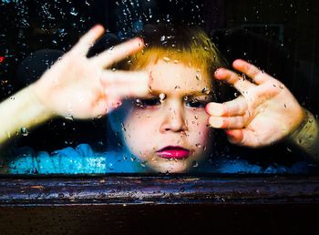 Sad boy looking through wet window