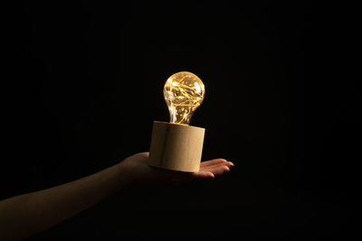 Close-up of hand holding light bulb against black background